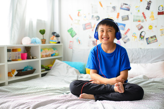 Little asian boy using headphones and smiling happy while listening music on bed