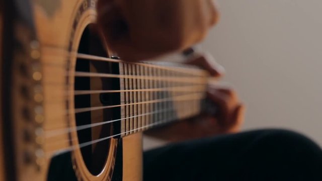 Close up shot of guitarist's hands plays chords on acoustic guitar at home