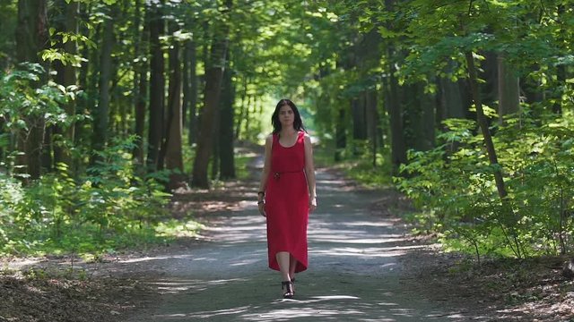Attractive woman in red dress walks forest, female in evening outfit, high heels