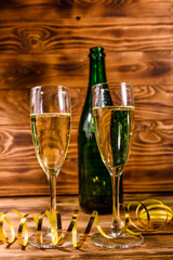 Bottle of champagne and two wineglasses decorated with golden ribbon on wooden table