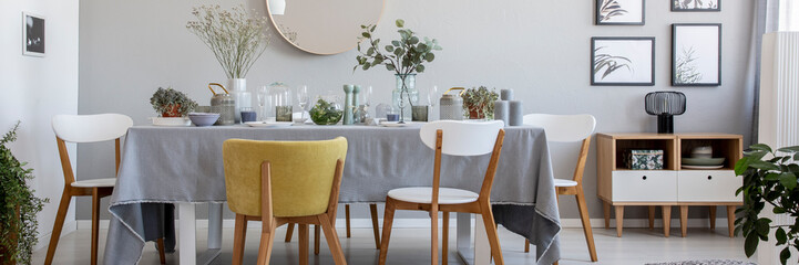 Modern chairs at table with flowers and tableware in grey dining room interior with posters. Real...