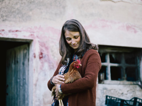 Smiling brunette woman holding chicken in her arms