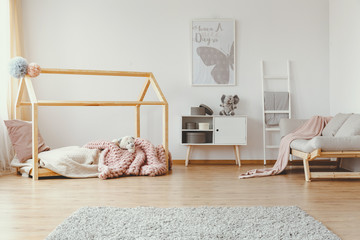 Scandinavian house shape bed with cozy pink blanket in bright bedroom with white furniture and...