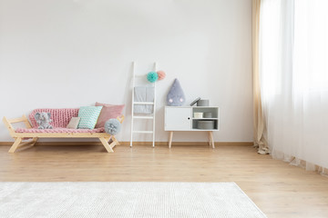 Comfortable sofa with pink blanket and colorful pillows next to white wooden ladder and shelf with...