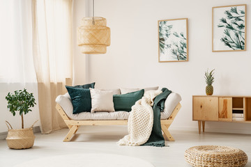 Stylish sofa with grey and green pillows and blankets in the middle of elegant white and bright living room