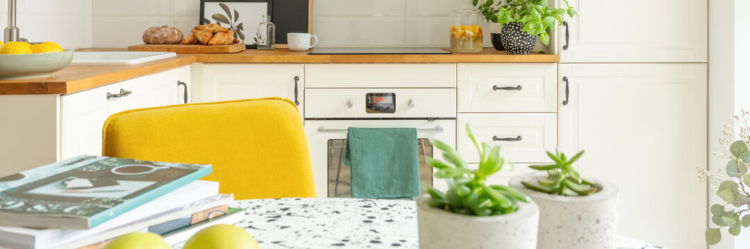 Closeup of stylish kitchen interior design with white cabinets, oven and yellow chair, panoramic view, real photo