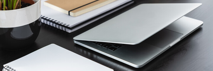 Real photo with close-up of silver laptop placed on black desk with notebooks