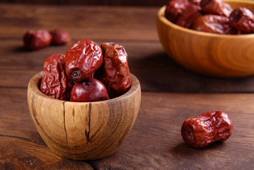 Red dry dates in a bowl on a wooden background.