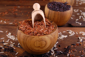 Brown, black and white rice in bowls on a wooden background.