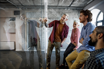 Group of casual young businesspeople having a working meeting in front of glass board.