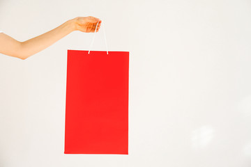 Cropped shot of female hand holding colorful red blank shopping bags over isolated white...