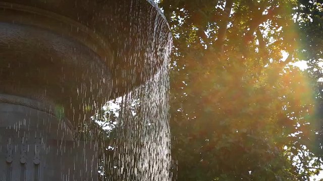 Drops of water pouring from a concrete city fountain close-up.
