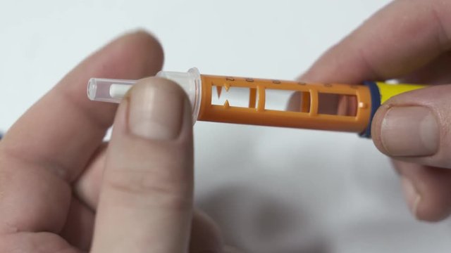 Insulin therapy routine. Patient with diabetes using diabetic insulin pen for self-injection. Attaching a new disposable needle to the pen before injecting
