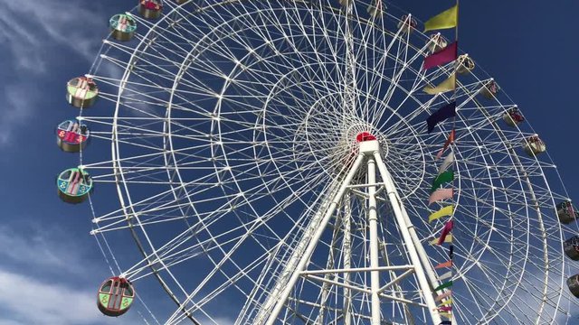 Ferris wheel attraction turning, flags fluttering in wind, city park to Krasnodar, daytime 4K.