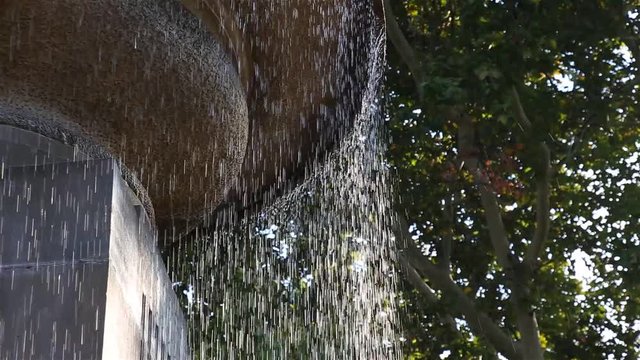 Drops of water pouring from a concrete city fountain close-up.