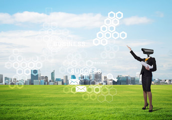 Camera headed woman standing on green grass against modern cityscape