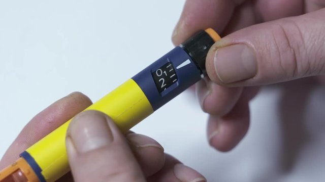 Insulin therapy routine. Patient with diabetes using diabetic insulin pen for self-injection. Turning the dosage knob to one or two units and removing air from new needle.