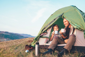 Family lisure concept image. Father and son drink a tea sitting in touristic tent