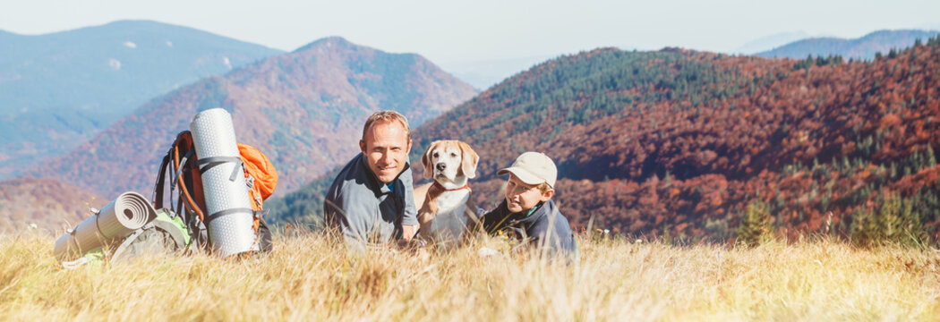 Father and son backpackers hikers rest on mountain hill with their beagle dog - Powered by Adobe