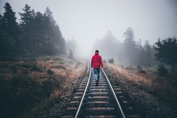 Wanderer läuft in roter Jacke über Schienen im Harz