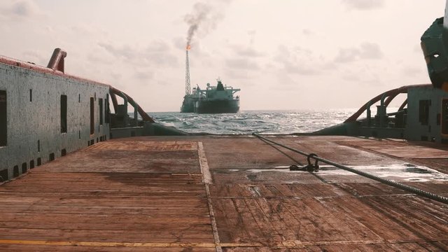 Anchor-handling Tug Supply AHTS vessel during dynamic positioning DP operations near FPSO tanker. Vessel is doing static tow tanker lifting. Ocean tug job.