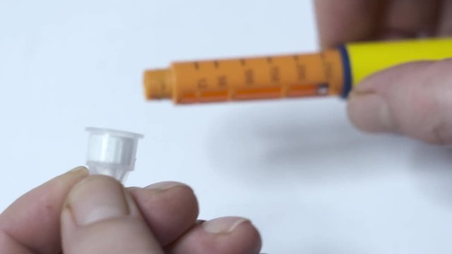 Insulin therapy routine. Patient with diabetes using diabetic insulin pen for self-injection. Attaching a new disposable needle to the pen and turning dial to the correct dose before injecting.