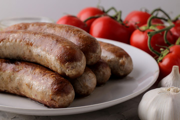Grilled sausages with tomatoes, sunflower oil and garlic on a light background