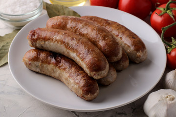 Grilled sausages with tomatoes, sunflower oil and garlic on a light background