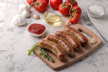Grilled sausages with a variety of vegetables tomatoes and garlic, red sauce and spices on a light background.
