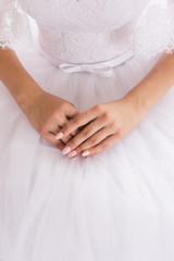 Well-groomed hands of the bride with a beautiful manicure are on a white wedding dress