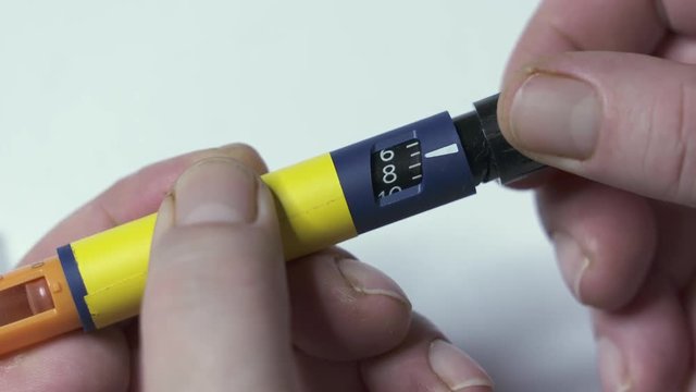Insulin therapy routine. Patient with diabetes using diabetic insulin pen for self-injection. Turning dial to the correct dose before injecting.