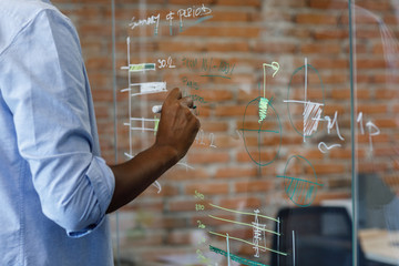 Hand of unrecognisable businessman writing data on glass board.