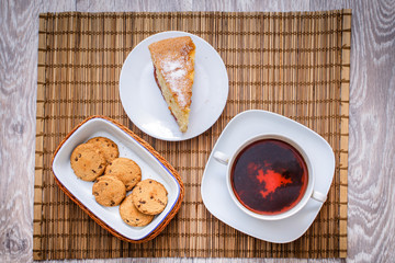 Plum biscuit cake for a cup of hot tea on a straw bedding with chocolate biscuits in a basket.