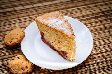 A piece of sponge cake On a round white plate with chocolate biscuits.
