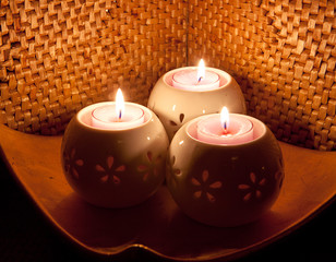 Three round creamy-white china candle holders with floral shaped cutouts and pink flickering candles.