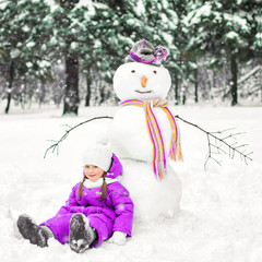 Fototapeta premium child and snowman in a snow-covered Park. winter outdoor activities