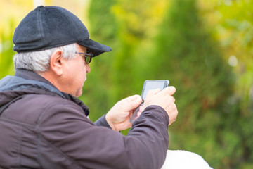 Portrait of an elderly man with glasses in the park. uses the phone. reads the message in social networks. old people and technology.