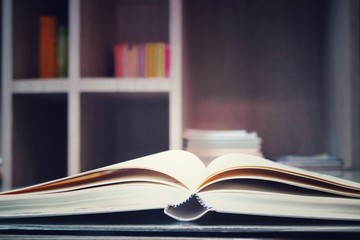 The old books open on the wooden table in the library. Selective focus with blurred bookshelves background. Vintage style picture. Education and book's day concept. 