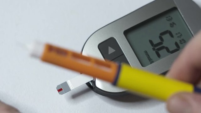 Diabetes testing equipment and insulin therapy. Patient with diabetes using a blood glucose meter and diabetic insulin pen for self-injection.