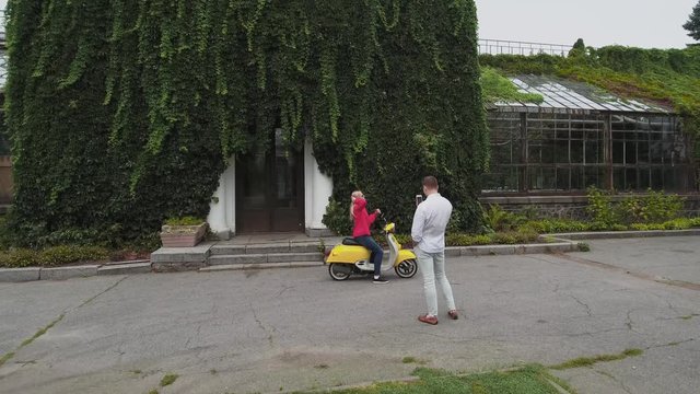 Guy takes a picture of a girl sitting on a scooter. Shot on drone