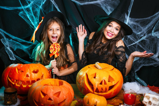 Happy Halloween. Beautiful caucasian mother and her daughter in witch costumes celebrating Halloween with Halloween candy and sweet over spider web