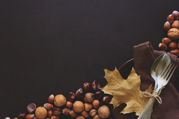 Tableware, walnuts, hazelnuts, chestnuts and acorns on dark wooden background. Thanksgiving day...