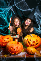 Fototapeta premium Happy Halloween. Beautiful caucasian mother and her daughter in witch costumes celebrating Halloween with Halloween candy and sweet over spider web