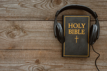 top view of holy bible with headphones on wooden surface