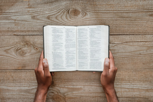 cropped shot of man holding holy bible over wooden table