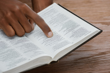 Naklejka premium cropped shot of african american man reading holy bible and pointing at psalm