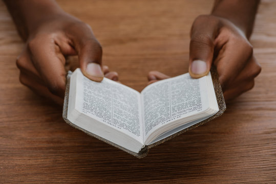 cropped shot of african american man reading holy bible on wooden table