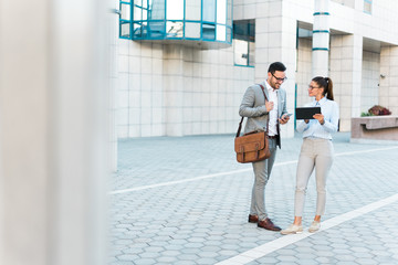 Team of two young successful happy business people working together, smiling, walking in the city, using phone and tablet.
