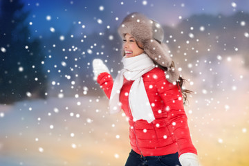 Fototapeta premium people, season and leisure concept - happy woman in winter fur hat having fun outdoors over evening background and snow