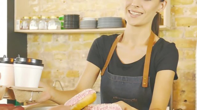 Smiling waitress giving cup of coffee and donats to the customer.